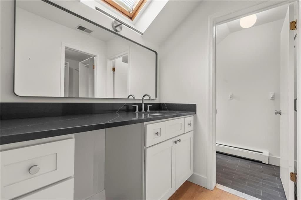 Eagle Bay primary vanity — a long honed stone counter beneath a skylight, with white shaker cabinetry