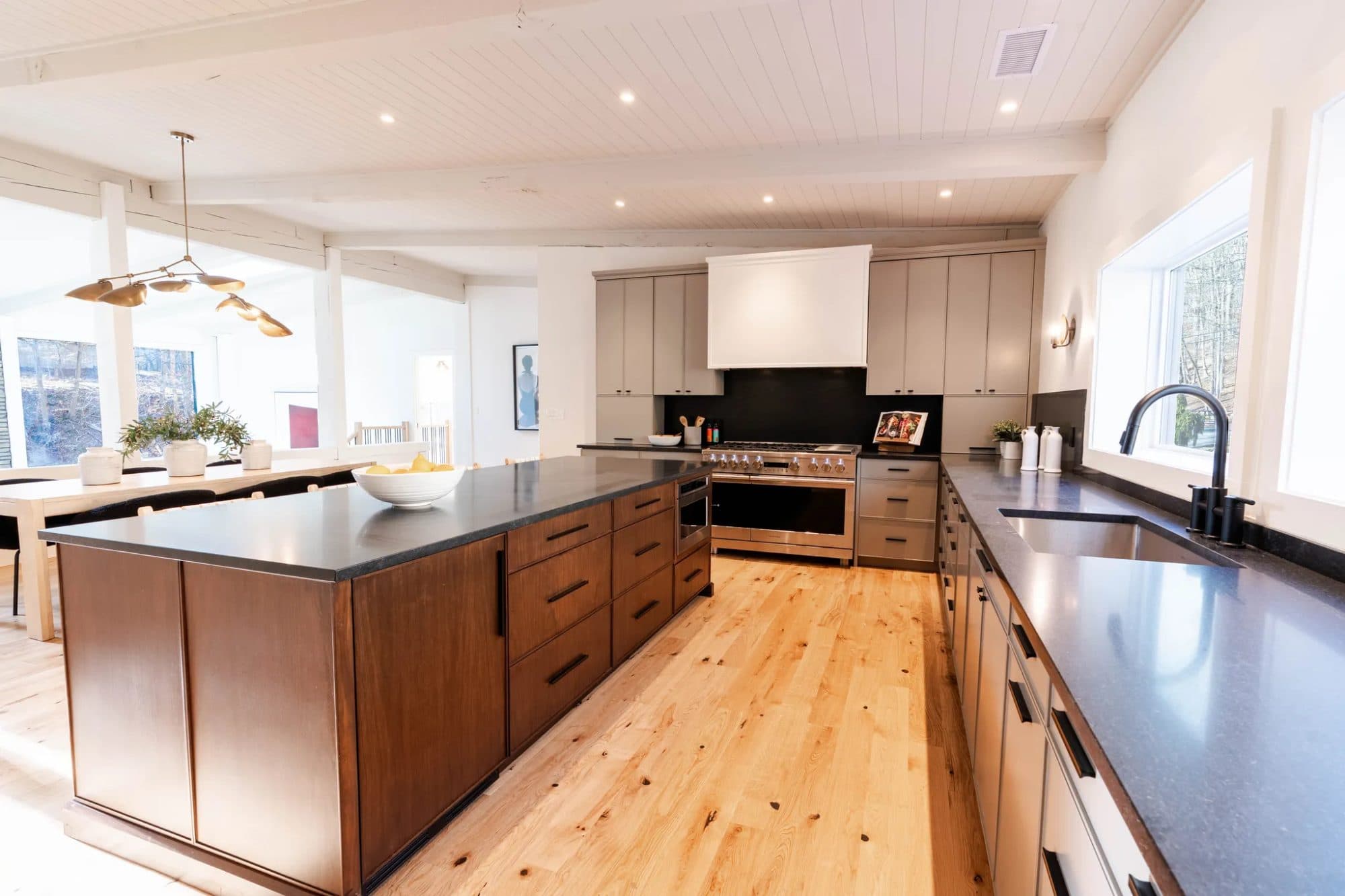Hawley kitchen — walnut island with honed black counters, woven stools, and windows to the trees