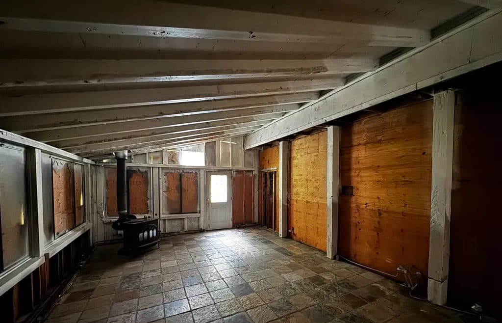 Hawley before — the fire-damaged interior stripped to studs and sheathing, with a wood stove remaining